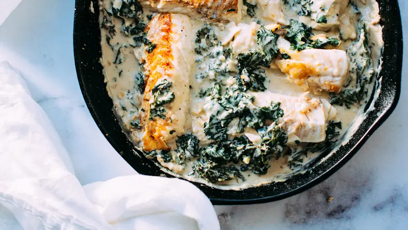 Fish fillets in a creamy kale sauce in a cast iron skillet on a marble counter